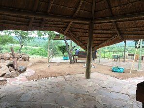 A covered outdoor area with stone flooring, wooden benches, and a thatched roof structure. - Paje River Camp (Paje)