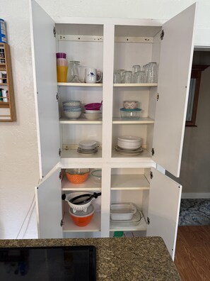 Un armari de cuina amb diverses prestatgeries que contenen diferents utensilis de cuina.