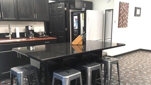 Une cuisine moderne avec des meubles de couleur sombre, un plan de travail noir et un réfrigérateur blanc. On y trouve trois tabourets et une machine à café sur le plan de travail.