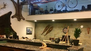 Un espace bar avec un mur en pierre, un jeu de fléchettes et des cannes à pêche.