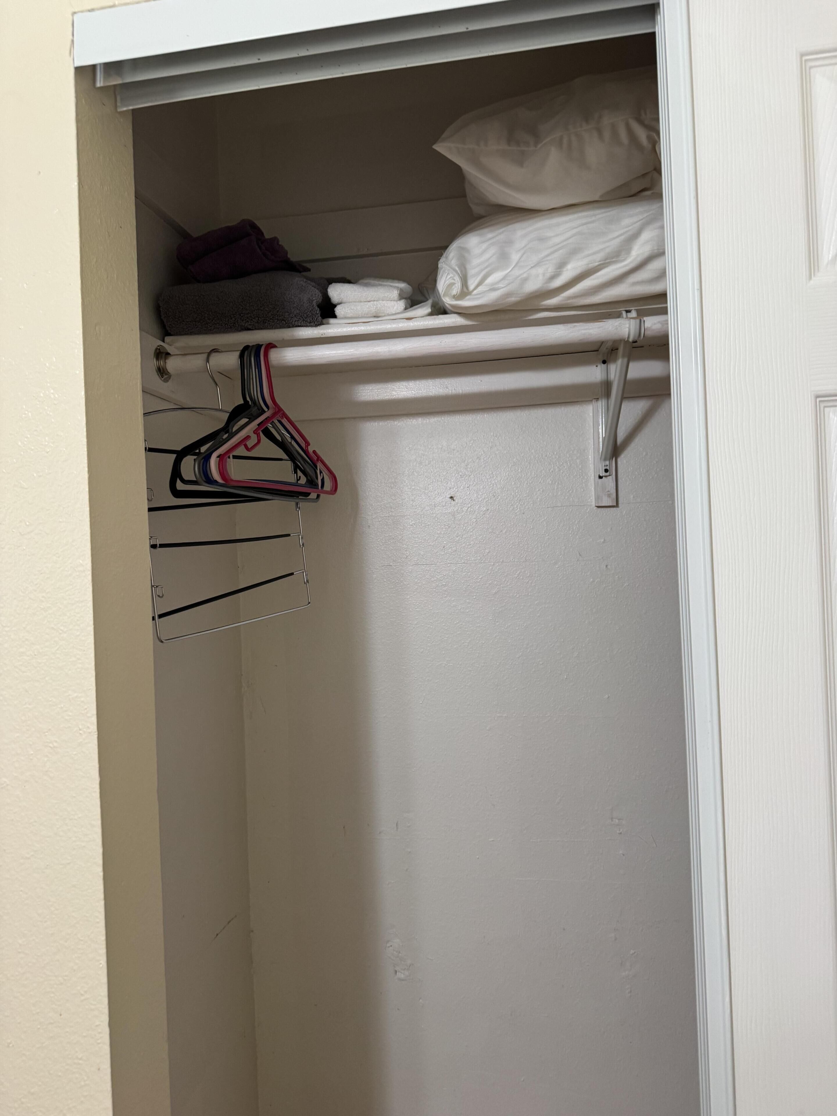A white closet with hanging clothes and a folded towel.