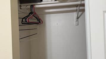 A white closet with hanging clothes and a folded towel.