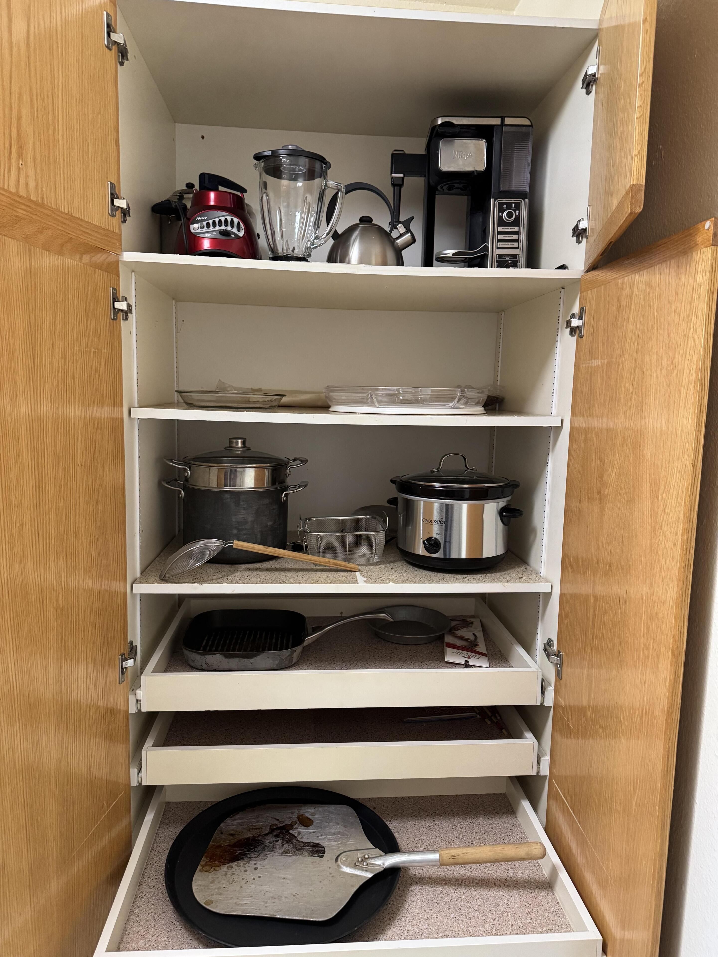 A kitchen with white cabinetry, a coffee maker, a blender, a kettle, pots, a strainer, a frying pan, and a spatula.
