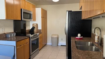 A kitchen with wooden cabinets, stainless steel appliances, a granite countertop, and a trash can.