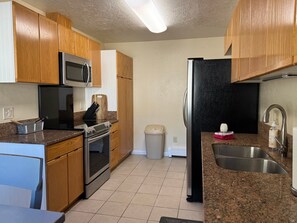 A kitchen with wooden cabinets, stainless steel appliances, a granite countertop, and a trash can. - Thunder Mountain Place - Quiet, Comfortable Place Offering DISCOUNT ON TOURS! (Juneau)