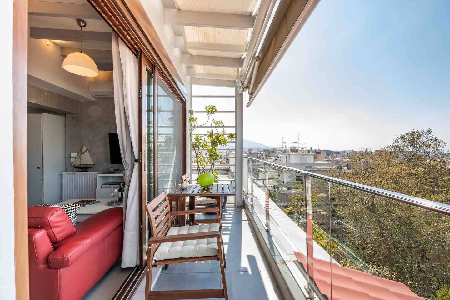 A balcony with a red sofa, a dining table with chairs, and a view of the cityscape.