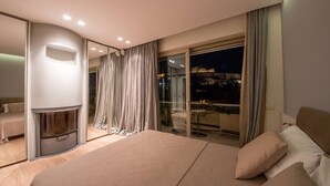 A modern bedroom with a large bed, a fireplace, and a balcony with a city view.