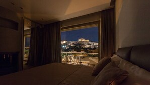 A hotel room with a balcony overlooking a cityscape at night, featuring a bed and a table with chairs.