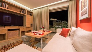 A modern living room with a sofa, a dining table set for two, a television, and a bookshelf.