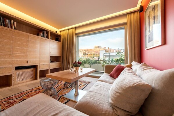 A modern living room with a sofa, coffee table, and bookshelf. A large window offers a view of the cityscape.