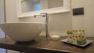 Een badkamer met een grote witte wastafel, een spiegel met een decoratieve lijst, een kraan, een zeepbakje en een dienblad met verschillende flessen vloeibare zeep.