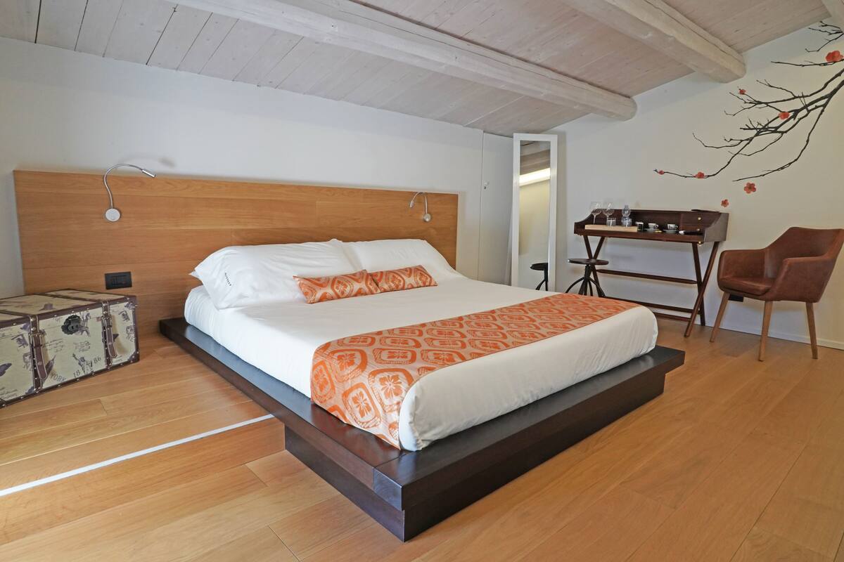 A bedroom with a wooden bed, a small table with glasses, and a chair.