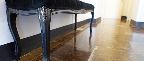 A bench with a cushioned seat and metal legs, positioned against a wall with a polished floor.
