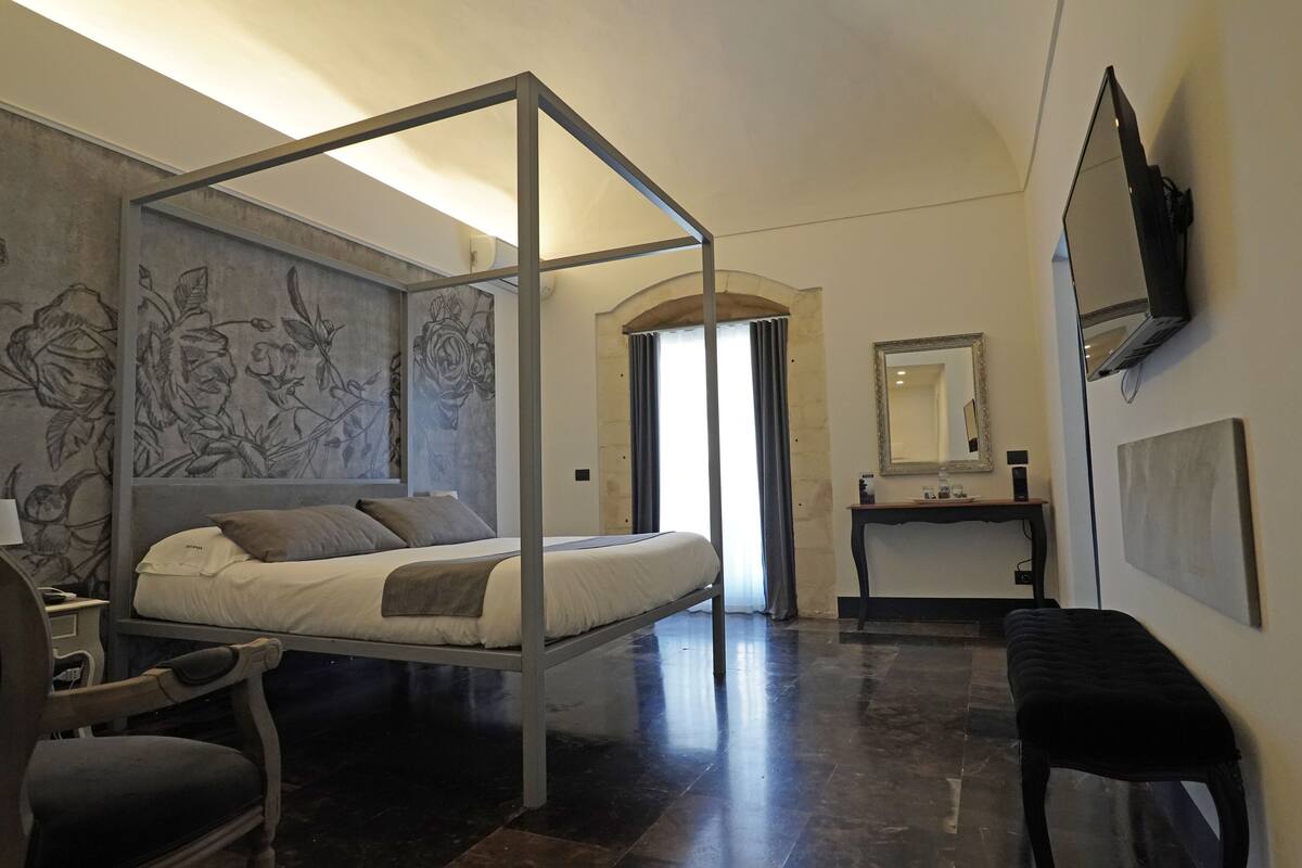 A modern bedroom with a four-poster bed, a desk, and a bench.