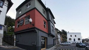 Un edificio de dos pisos con fachada roja y gris, un letrero de tienda visible y una vista de la calle con coches estacionados.