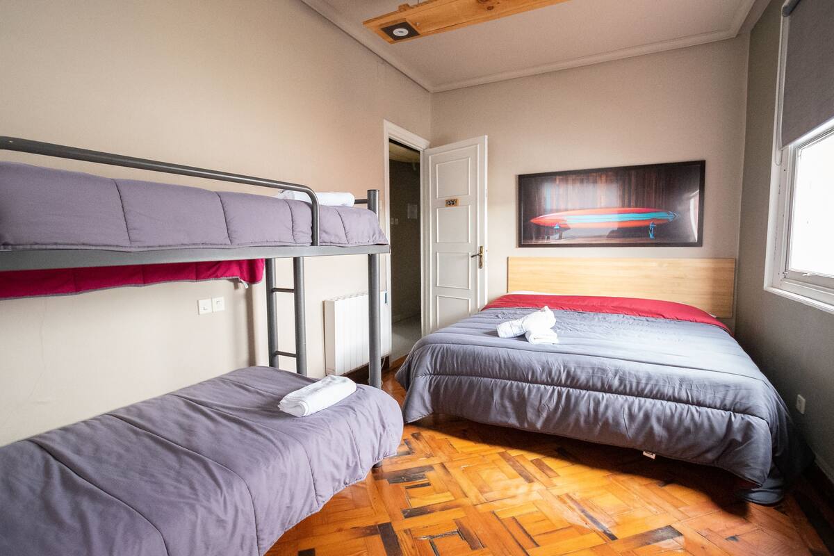 Ein Schlafsaalzimmer mit zwei Einzelbetten, Holzboden, einer Tür und einem Bild an der Wand.