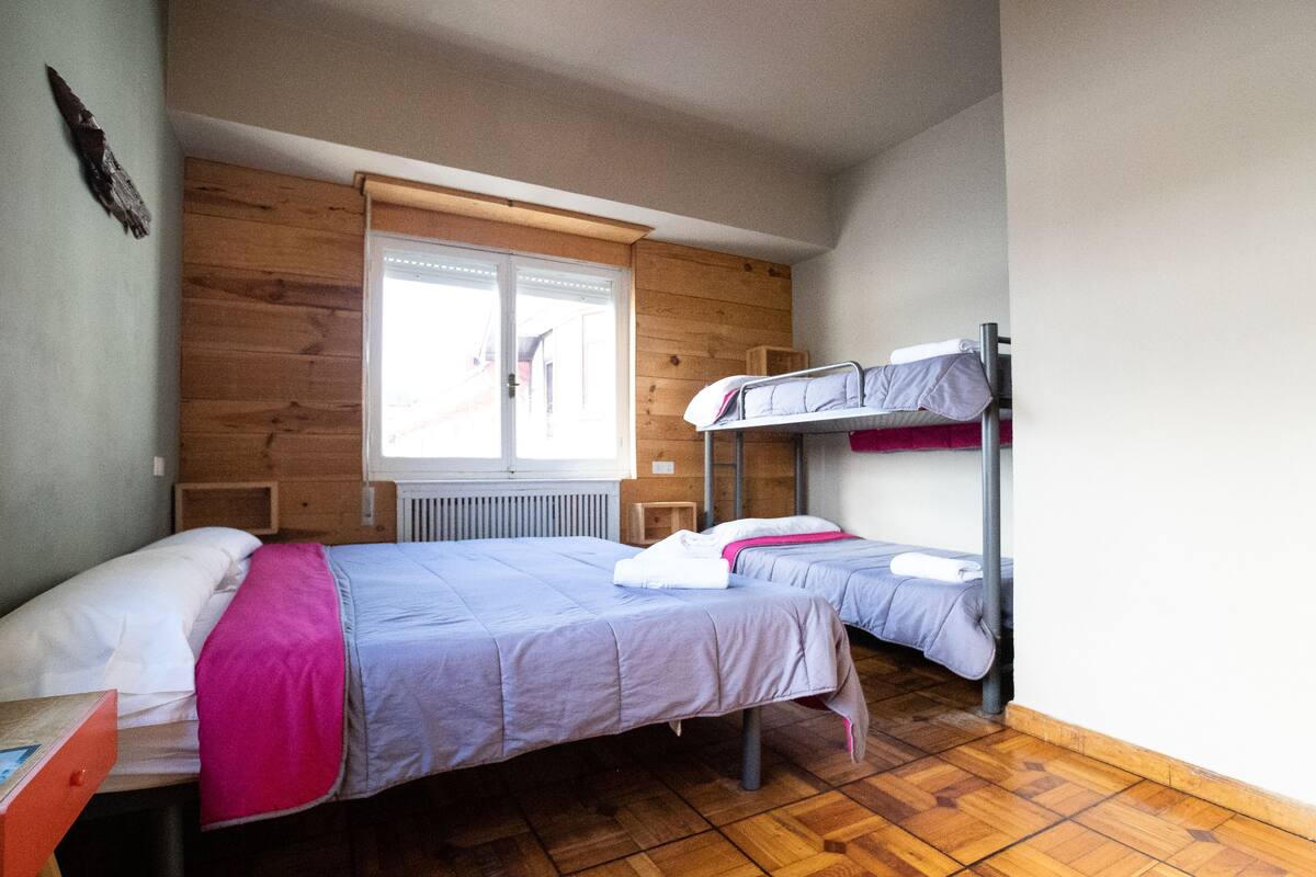 Ein Schlafsaalzimmer mit zwei Betten, Holzwänden, einem Fenster und einer Heizung.