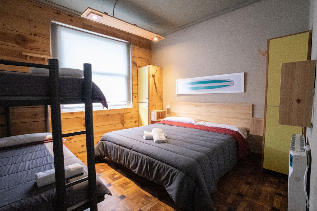 Ein Zimmer mit Etagenbetten, einem Holzschrank, einem Bett mit roter Decke und einem an der Wand montierten Regal.