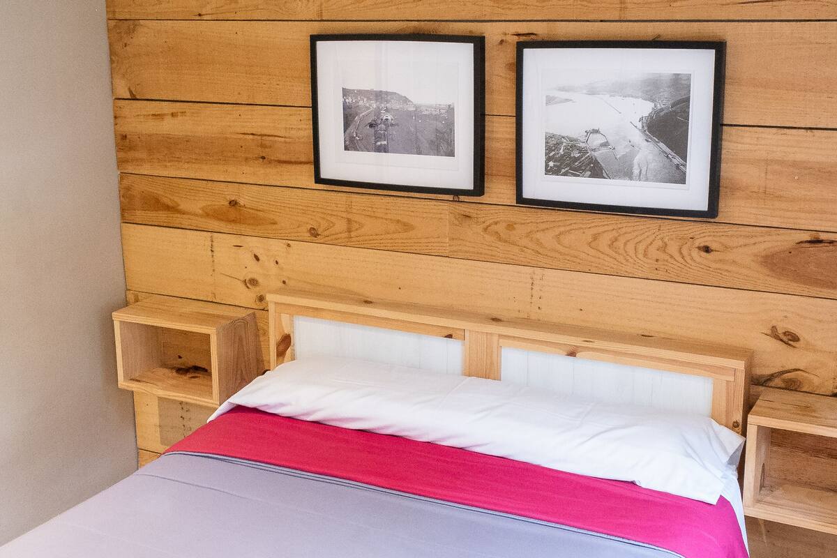 Ein ordentlich bezogenes Bett mit einer rosa Decke und weißen Kissen, einem Holzkopfschild und zwei gerahmten Bildern an der Wand.