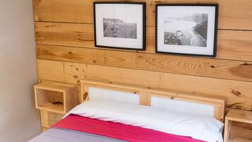 Un lit bien fait, avec une couverture rose et des oreillers blancs, une tête de lit en bois et deux tableaux encadrés accrochés au mur.