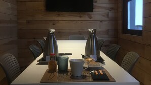 Un salón de conferencias con una mesa larga, sillas, un televisor montado en la pared y un ventanal con luz natural.