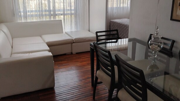 A living room with a glass dining table, wooden floor, white sofa, and a ceiling fan.