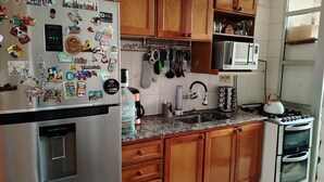 A kitchen with wooden cabinets, a stainless steel refrigerator, a microwave, a sink, and a stove.