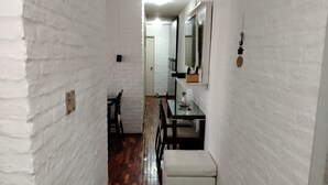 A hallway with white brick walls, wooden flooring, and a bench. There is a mirror on the wall and a door at the end of the hallway.