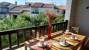 Ein Holztisch ist gedeckt mit einer Vase, Tellern und Tassen auf einem Balkon mit Blick auf Häuser und Grünflächen.
