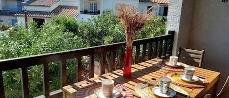 A wooden table set with a vase, plates, and cups on a balcony with a view of houses and greenery.