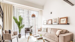 Un salon moderne avec un canapé, des fauteuils, une table basse et une grande fenêtre agrémentée de rideaux.
