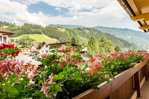 A balcony with wooden railings overlooking a village with houses and mountains in the background.
