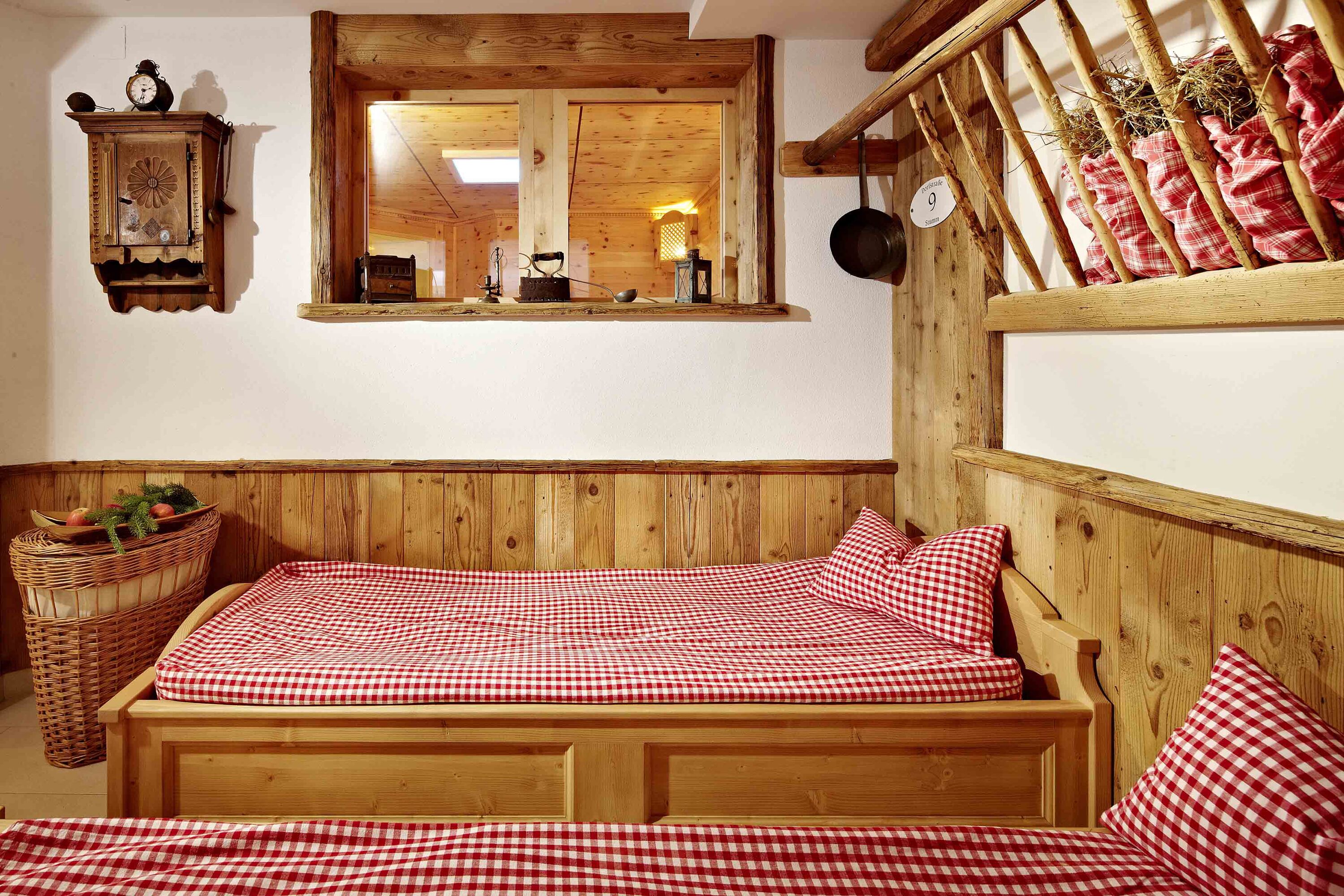 Una cama de madera con ropa de cama a cuadros, un cabecero de madera, un espejo, un reloj y una cesta con frutas.