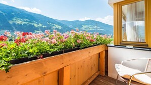 Un balcon avec des balustrades en bois, une chaise en osier et un jardinier contenant des fleurs roses et rouges.