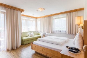 A hotel room with a wooden bed, a green sofa, a small round table, and a lamp. - Hotel Riedl (Stumm)