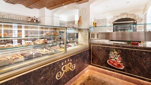 Une vitrine de boulangerie présentant diverses pâtisseries et desserts, un comptoir en marbre orné d’un logo et, au fond, un four en pierre.