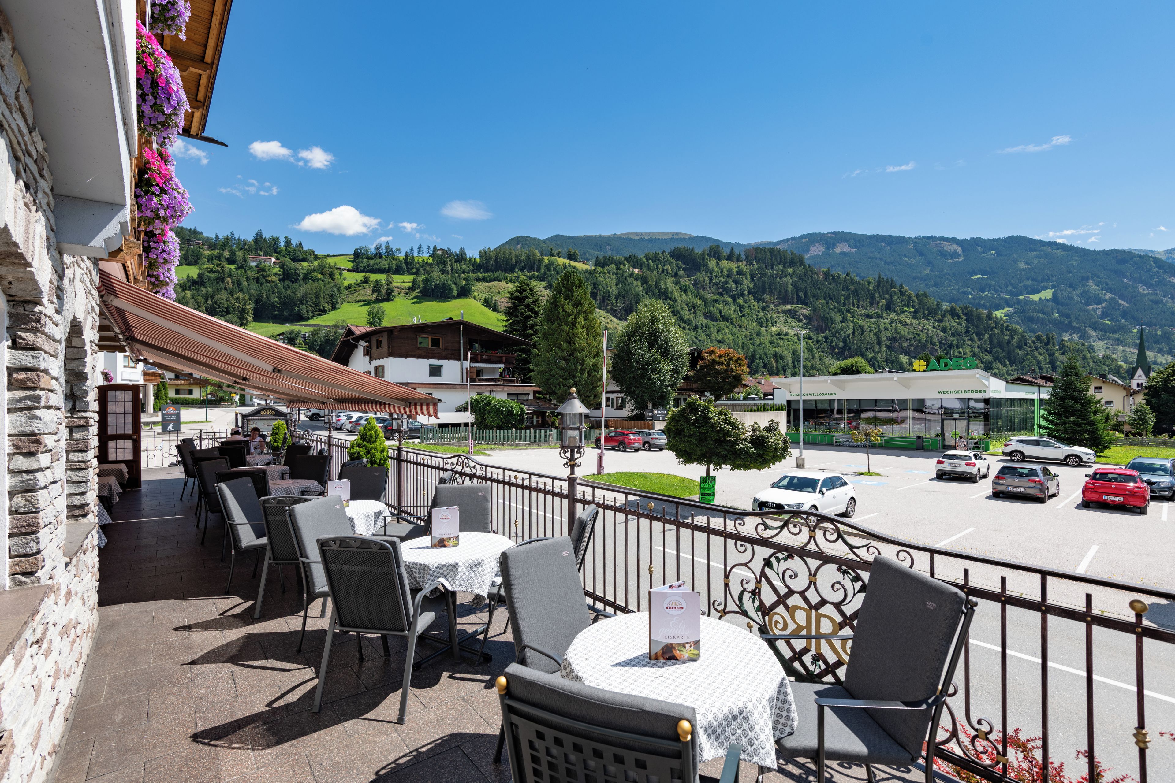 Una terraza con asientos al aire libre, vistas a un estacionamiento y montañas al fondo.