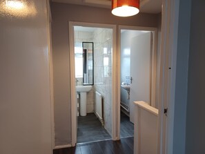A narrow hallway leading to a bathroom with white tiles, a sink, and a mirror. - Poynters House - Huku Kwetu Luton (Luton)