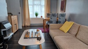 A living room with a chessboard, a sofa, a coffee table, a fireplace, and a window with curtains. - Poynters House - Huku Kwetu Luton (Luton)