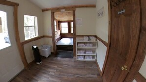 Une pièce avec un plancher en bois, une porte en bois portant l’inscription « TOILETTES », une fenêtre et une étagère avec des serviettes pliées.