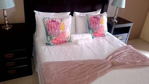 Una cama bien hecha con almohadones estampados, un cabecero oscuro y mesitas de noche con lámparas.