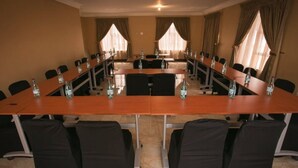 Un salón de conferencias con una mesa larga, sillas negras y botellas de agua.