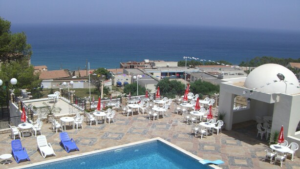 Un espace piscine avec des chaises longues et des parasols, une structure en forme de dôme blanc et une vue sur la mer.