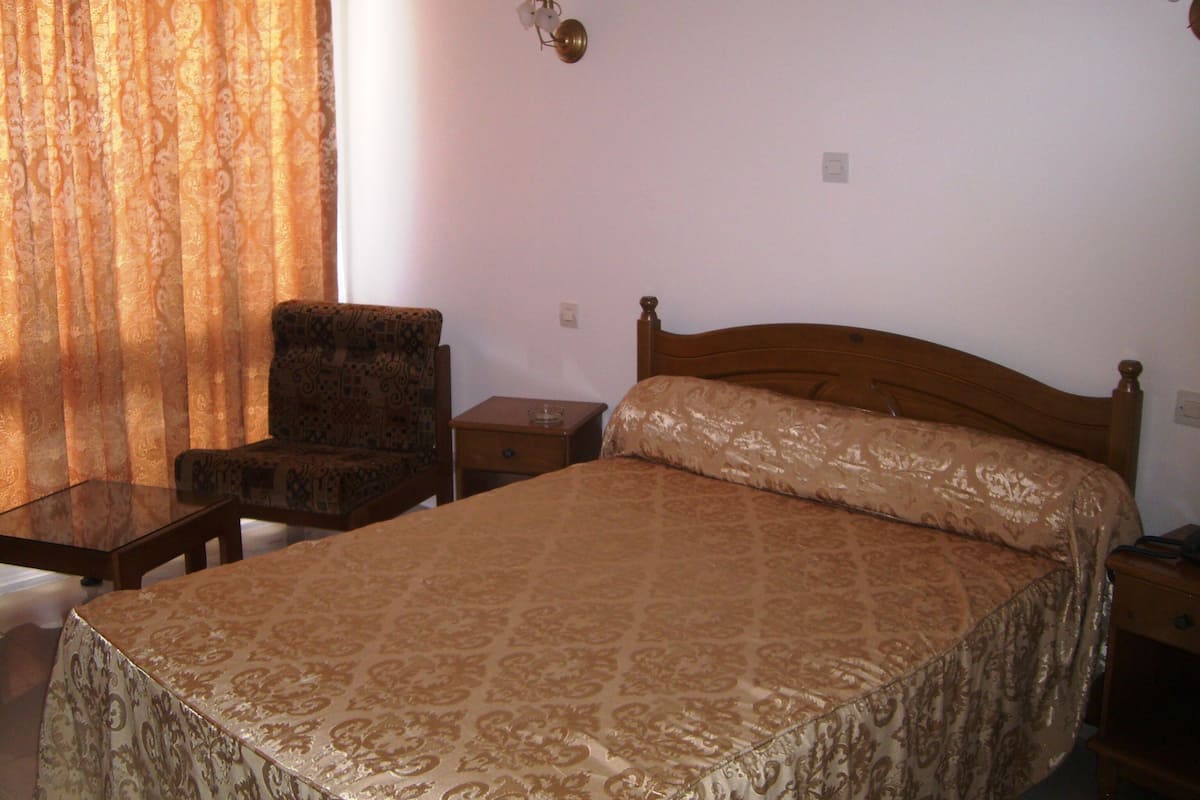 Une chambre à coucher avec un lit, une chaise, une table de chevet et une lampe.