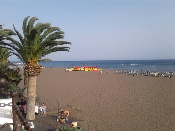 Una playa con palmeras, una fila de sombrillas de colores y una vista despejada del mar.