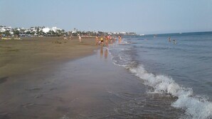 A beach with people walking along the shore and a clear sky.