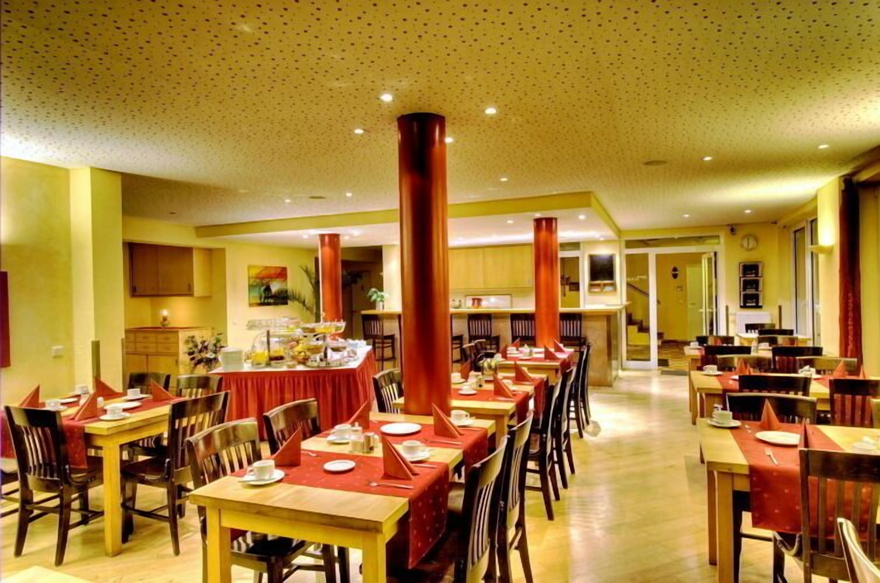 A spacious dining area with multiple tables and chairs, a high ceiling with a dotted pattern, and a warm color scheme.