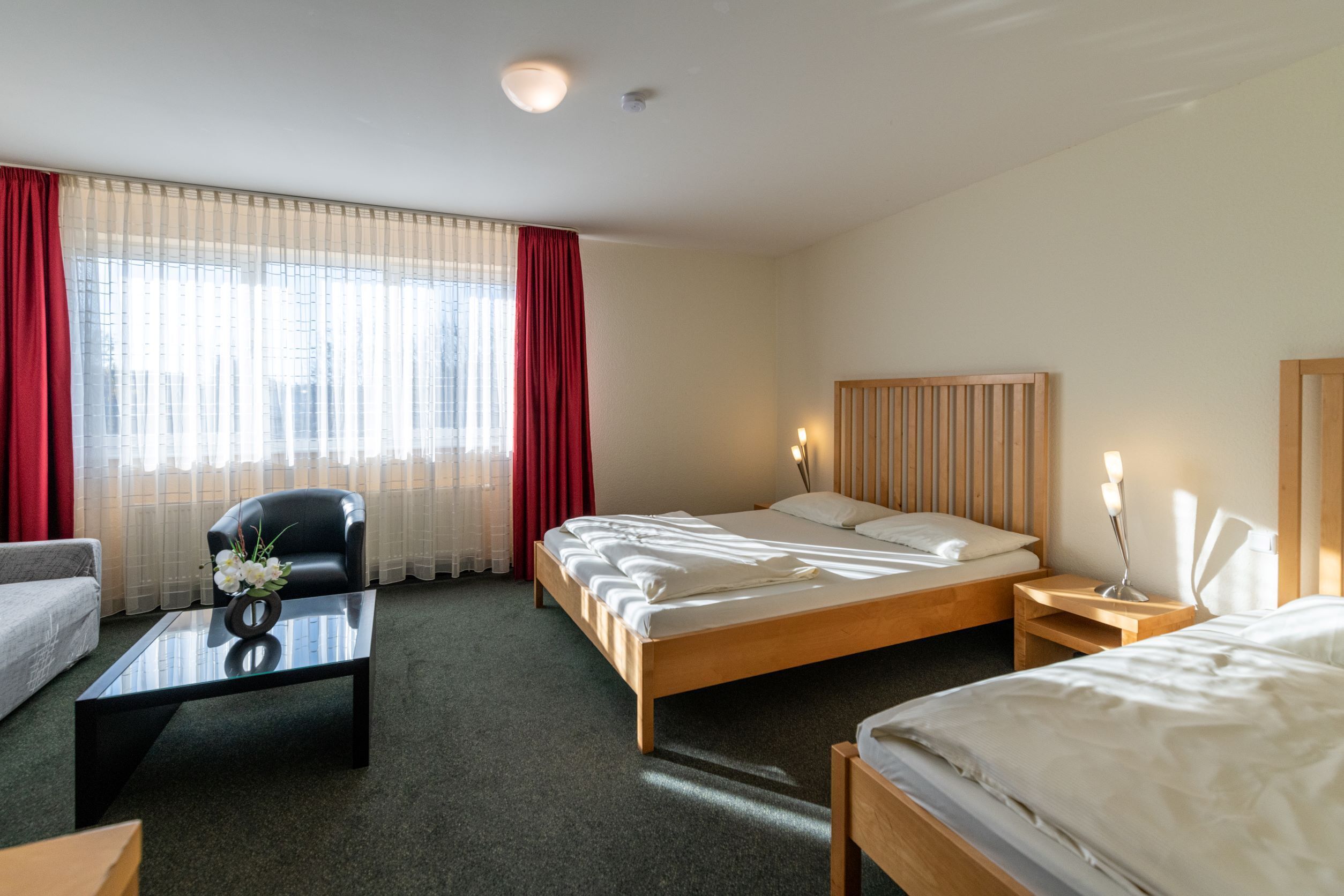 A hotel room with a bed, a chair, a small table with a vase of flowers, and a bedside table with a lamp.