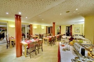 Un comedor con varias mesas y sillas, un bufé con diversas opciones de comida, y un techo con un diseño moteado.