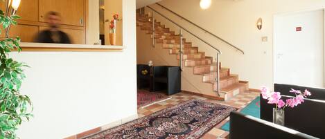 A spacious living area with a large rug, a staircase, and a door with a sign.